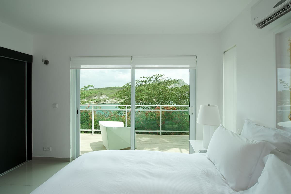 A bedroom with a large bed, a balcony with a table, and a painting on the wall.