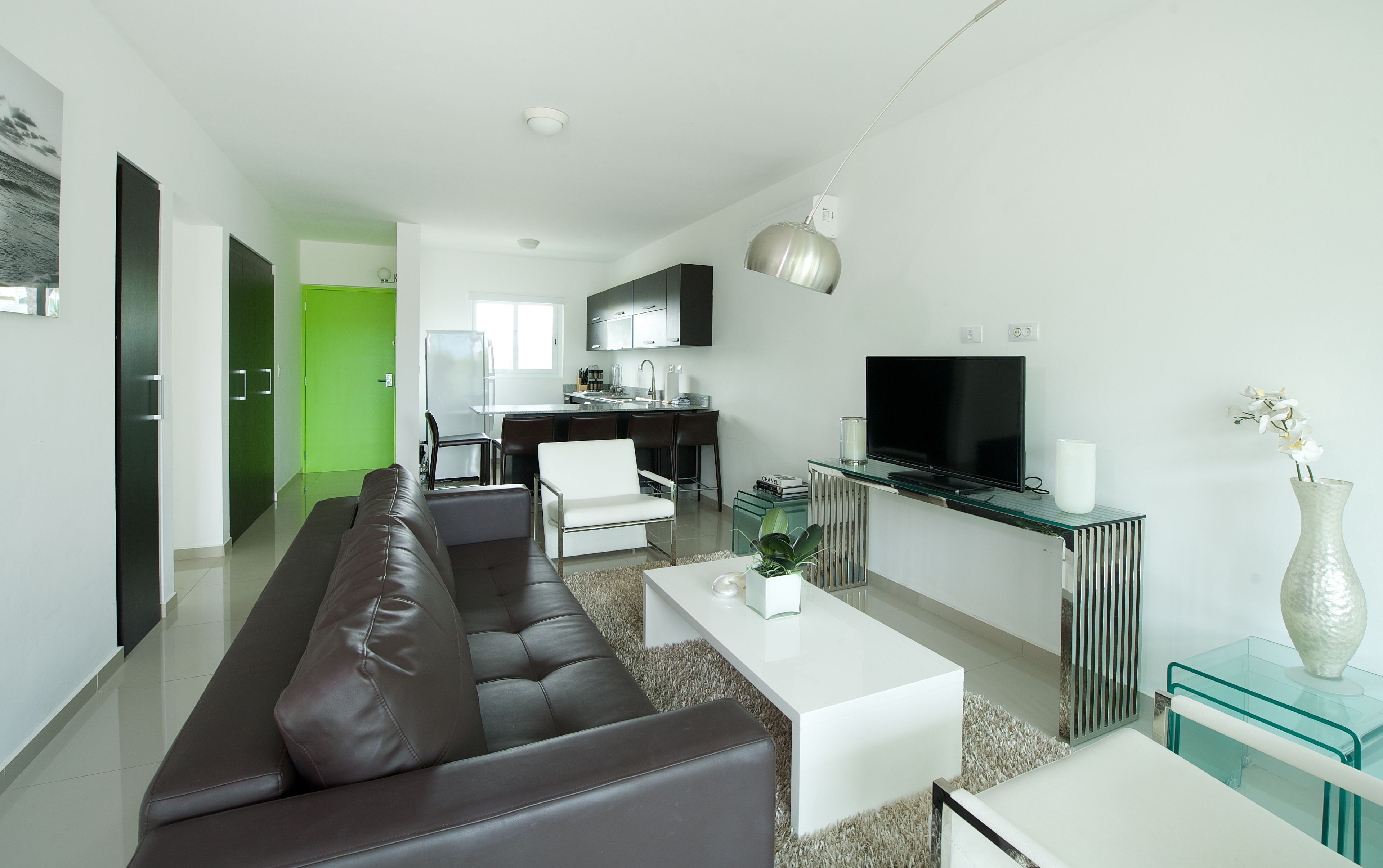 Una sala de estar moderna con un sofá de cuero marrón, una mesa de centro blanca y un mueble para televisión de vidrio.