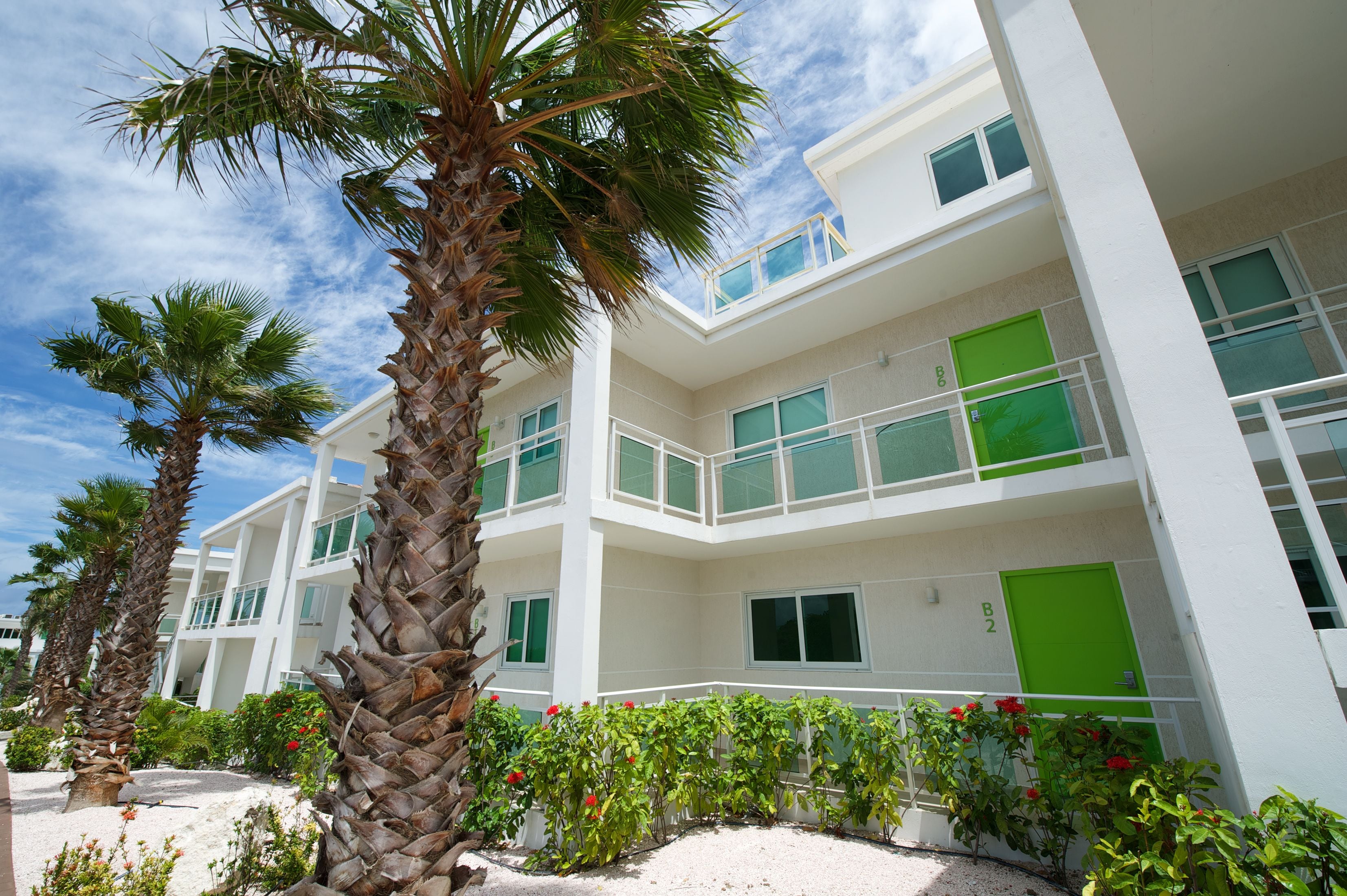 A multi-story hotel with balconies, palm trees, and red flowers.