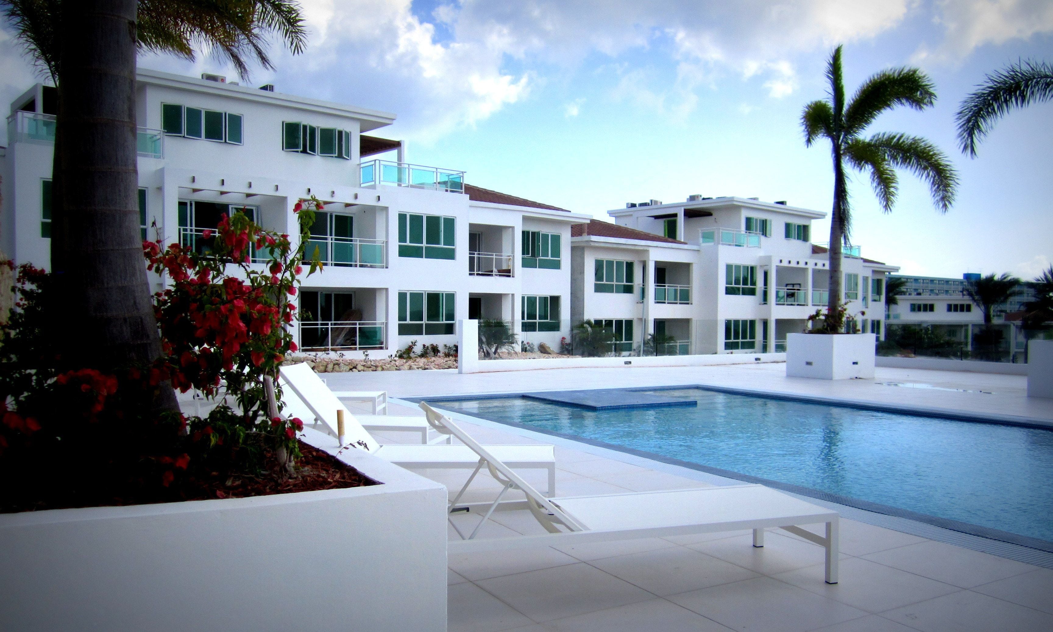 A modern hotel with a pool, white exterior, and balconies.