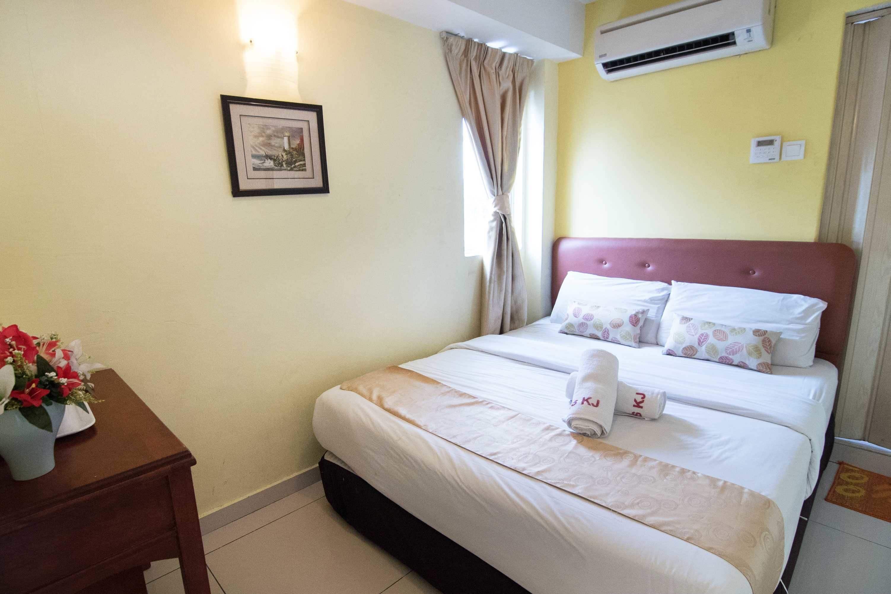A hotel room with a bed, a bedside table with a vase of flowers, an air conditioning unit, and a framed picture on the wall.