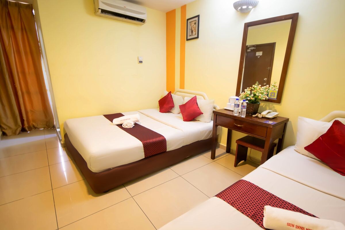 A hotel room with two beds, a bedside table with a phone, a mirror, and a window with curtains.