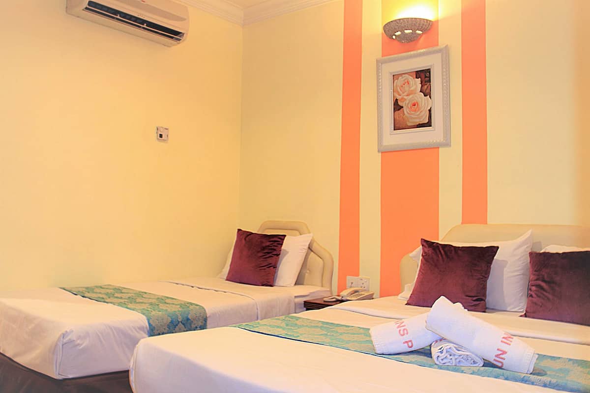 A hotel room with two single beds, each with a pillow and a blanket. There is a wall-mounted air conditioner and a framed picture on the wall.