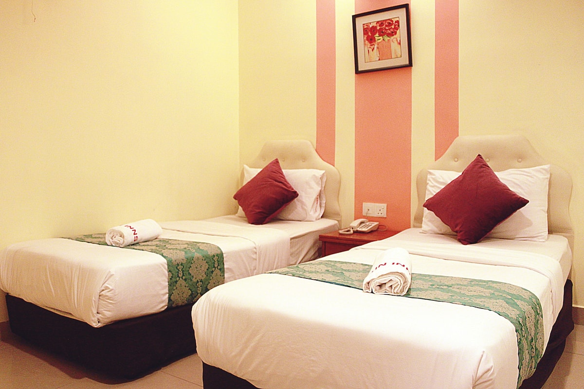 A hotel room with two beds, each with a pillow and a rolled towel.
