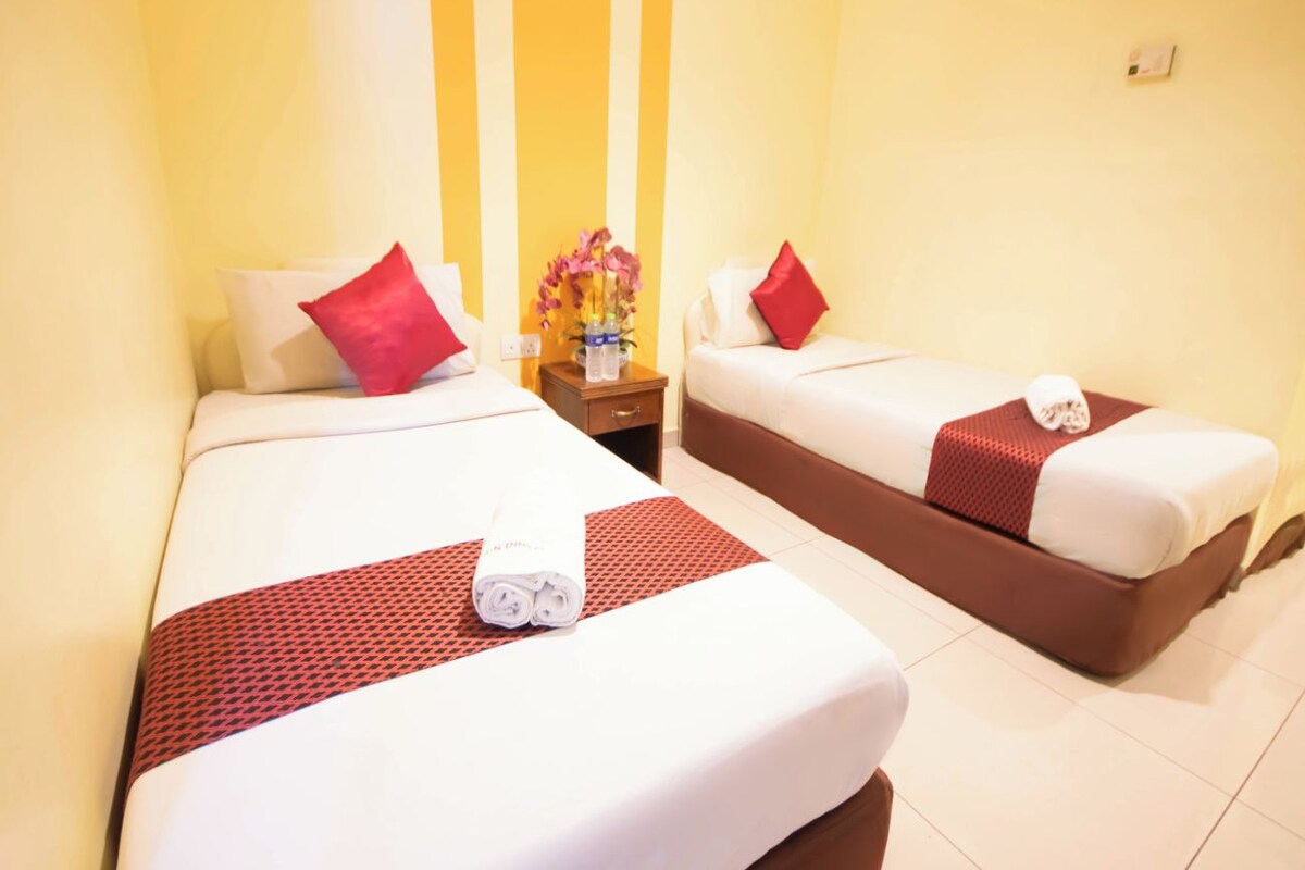 Una habitación de hotel con dos camas, cada una con una colcha roja y blanca, un almohadón rojo y una toalla blanca enrollada sobre la cama.