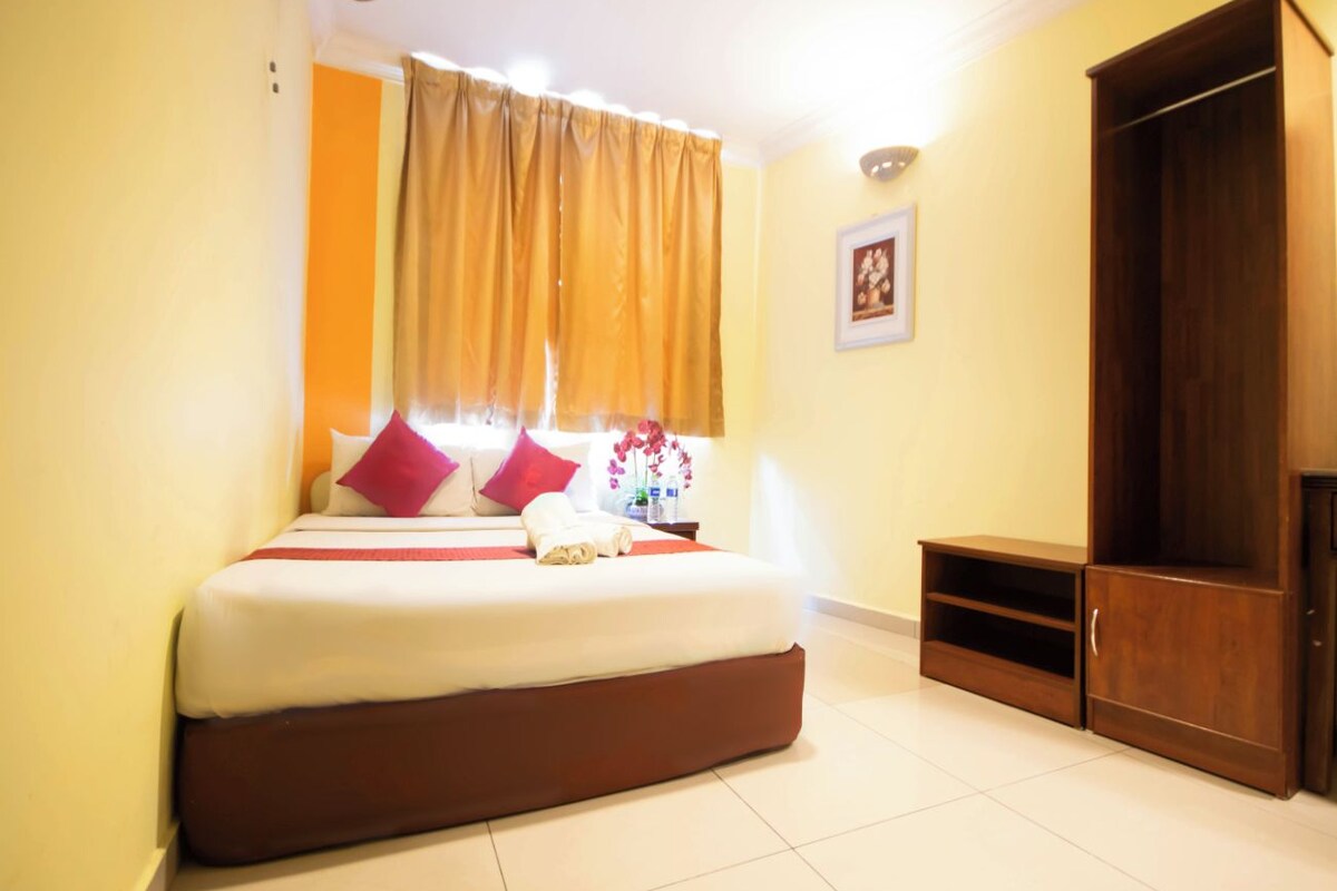 Habitación de hotel con cama, armario de madera, mesita de noche y ventana con cortinas.