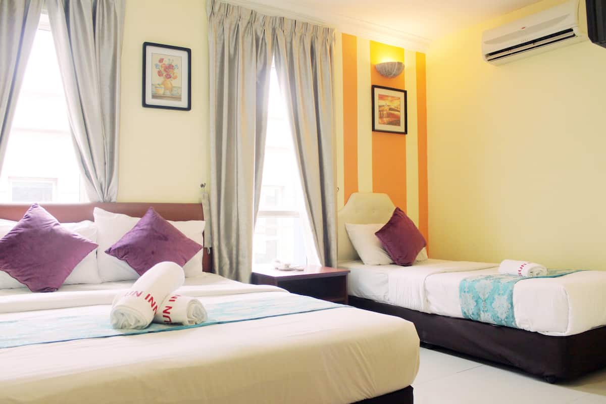 A hotel room with two beds, a nightstand, a wall-mounted air conditioner, and a window with curtains.