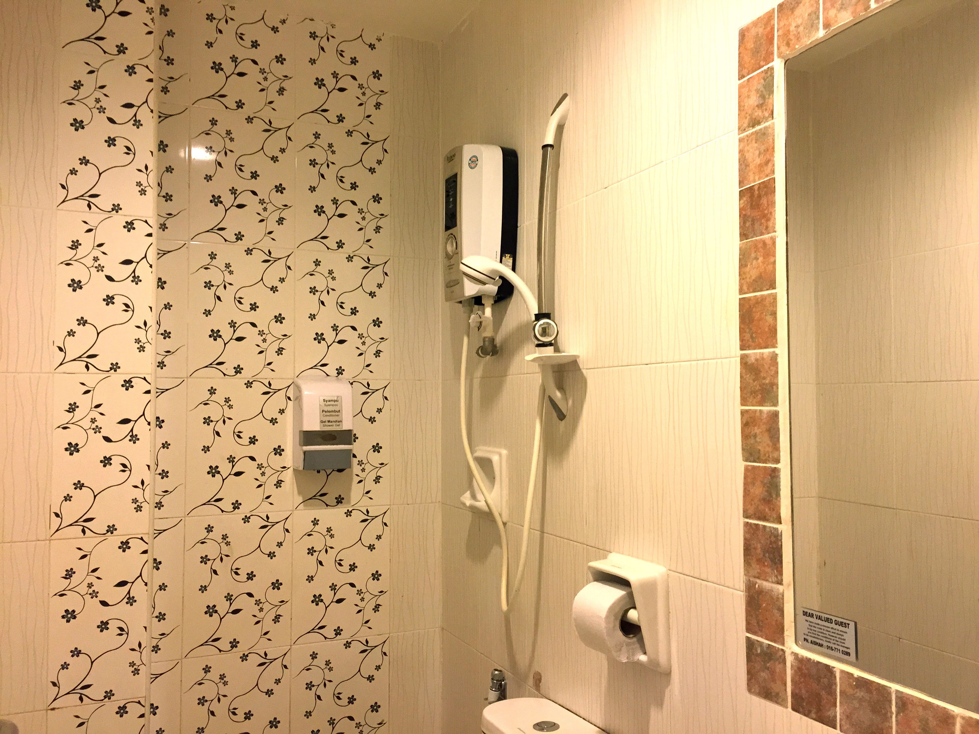 A bathroom with floral patterned tiles, a toilet, a hand dryer, and a paper towel dispenser.