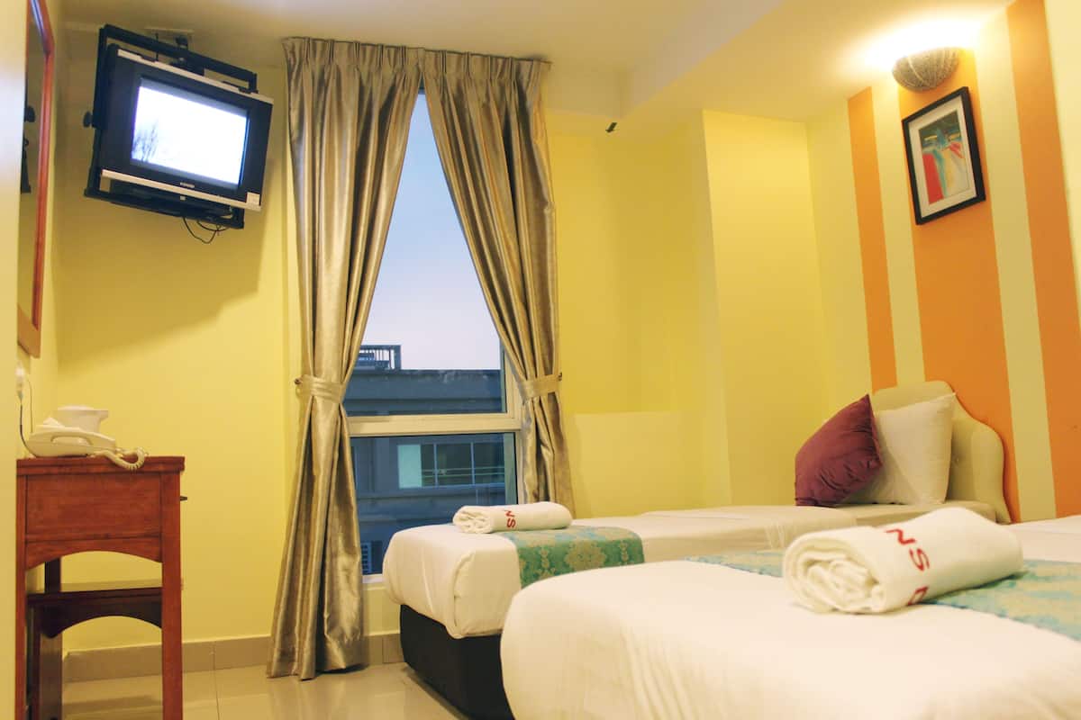 A hotel room with two beds, a TV mounted on the wall, a bedside table with a phone, and a window with curtains.