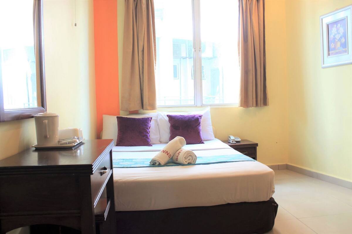 A hotel room with a bed, a bedside table, a window with curtains, and a wall-mounted phone.