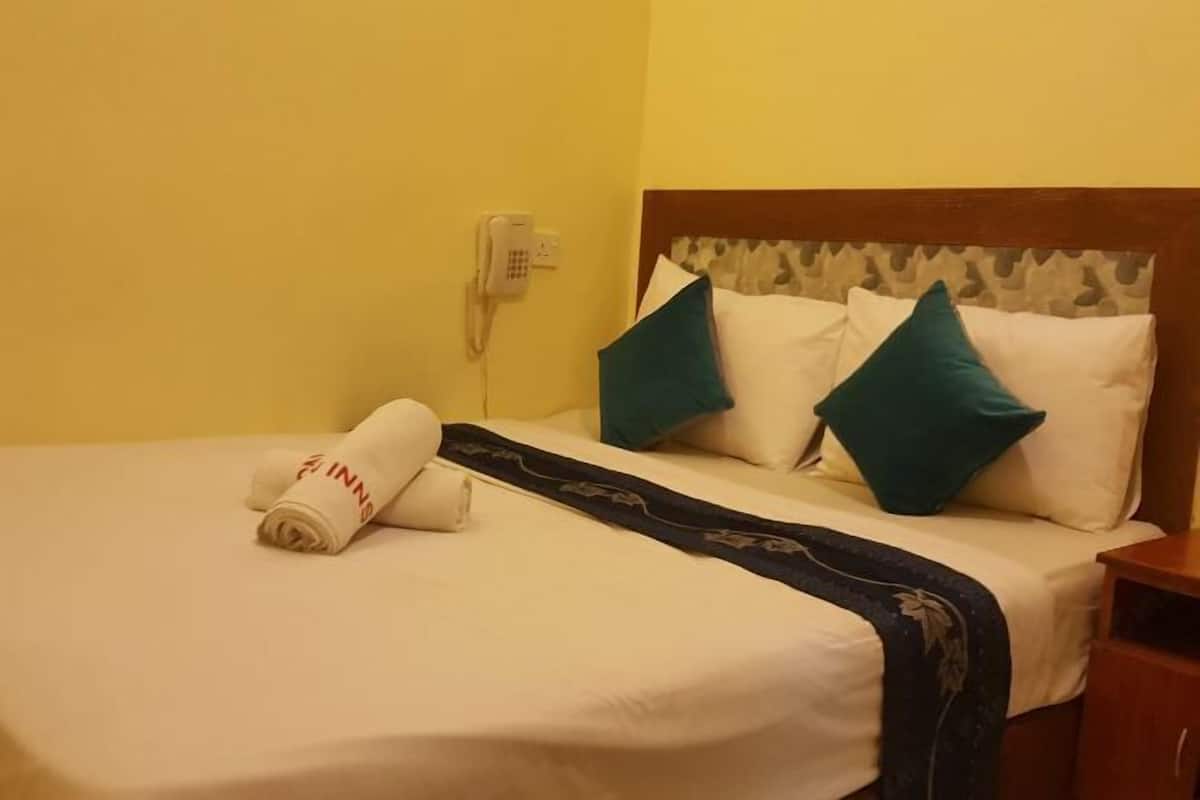 Une chambre d’hôtel avec un lit bien fait, un téléphone fixé au mur et une table de chevet en bois.