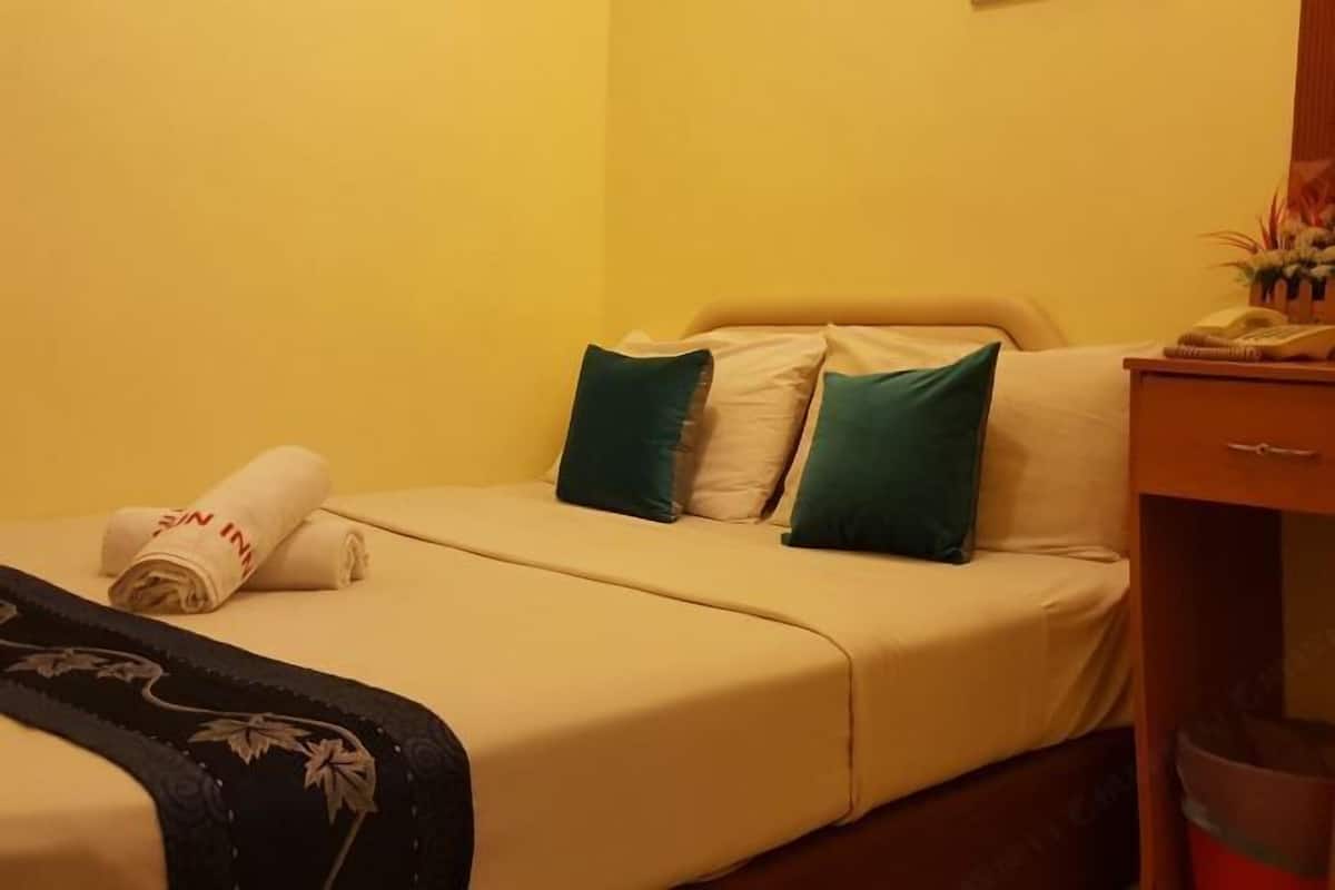 Une chambre d’hôtel avec un lit, des oreillers, une serviette roulée, un téléphone et une poubelle.