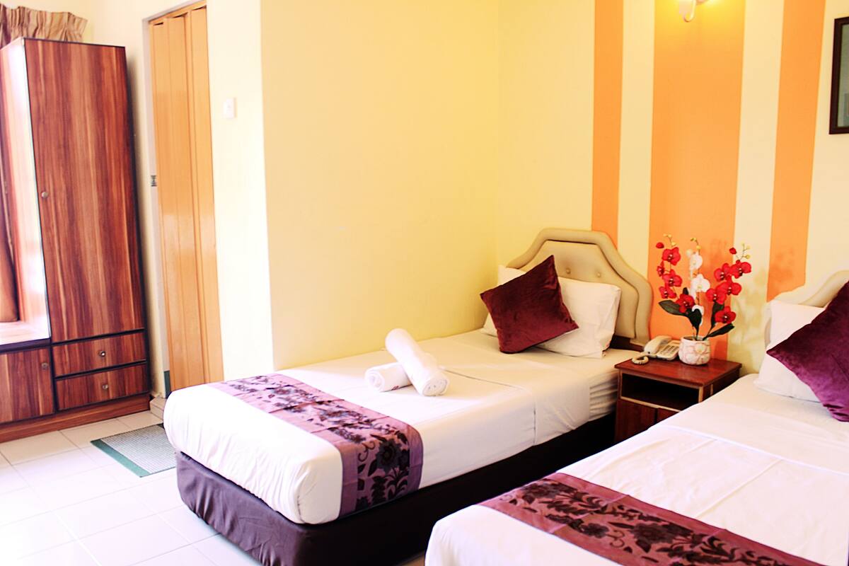 A hotel room with two beds, a wardrobe, a nightstand with a phone, and a vase with flowers.
