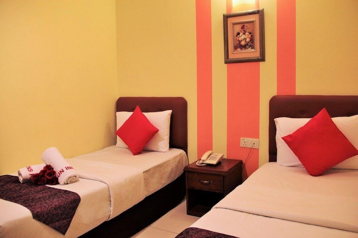 Une chambre d’hôtel avec deux lits, chacun agrémenté d’un oreiller rouge, une table de chevet avec un téléphone et un tableau accroché au mur.