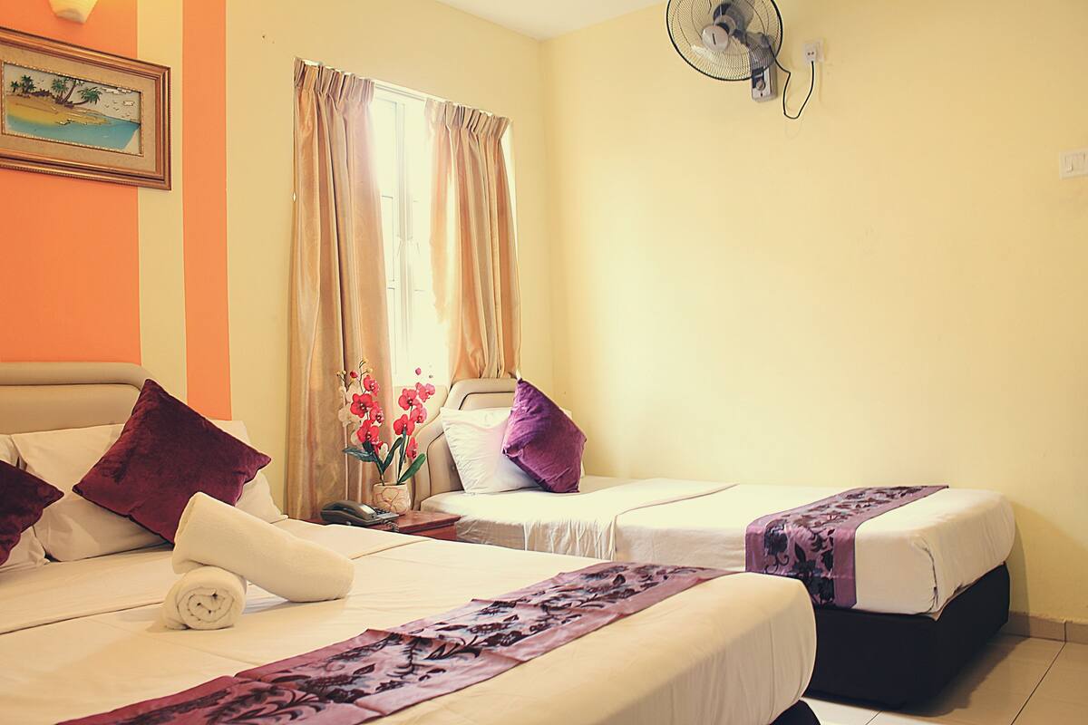 A hotel room with two beds, a fan, a window with curtains, and a painting on the wall.