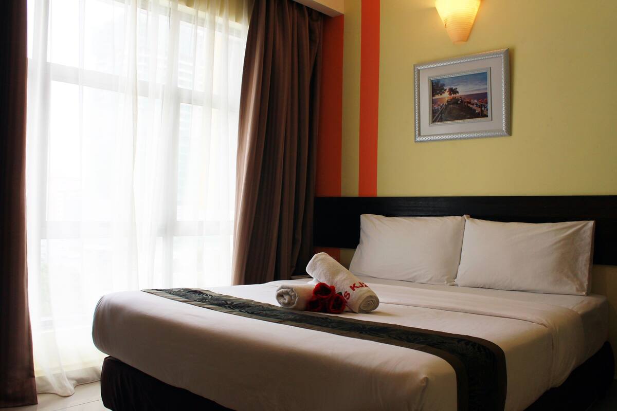 A hotel room with a bed, a framed picture on the wall, and a window with curtains.