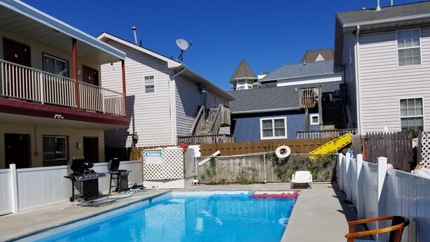 A swimming pool with a wooden deck, a white chair, and a warning sign on a fence.
