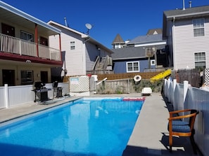 A swimming pool with a wooden deck, a white chair, and a warning sign on a fence. - Flamingo Inn (Seaside Heights)