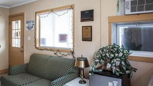 A room with a patterned sofa, a lamp, a potted plant, and a window with blinds.