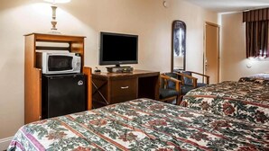 A hotel room with a bed, a desk with a television, a microwave, a chair, and a mirror.