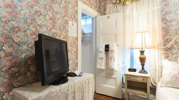 A room with floral wallpaper, a television on a small table, a bedside lamp, and a door leading to another room.