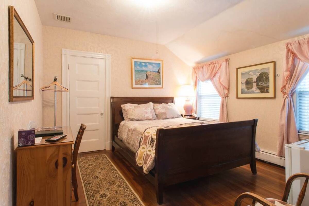 Una camera da letto con un letto in legno, una scrivania con una sedia, una porta e due quadri appesi al muro.