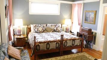 A bedroom with a wooden four-poster bed, two bedside tables, a nightstand, a dresser, a window with curtains, and a painting on the wall.