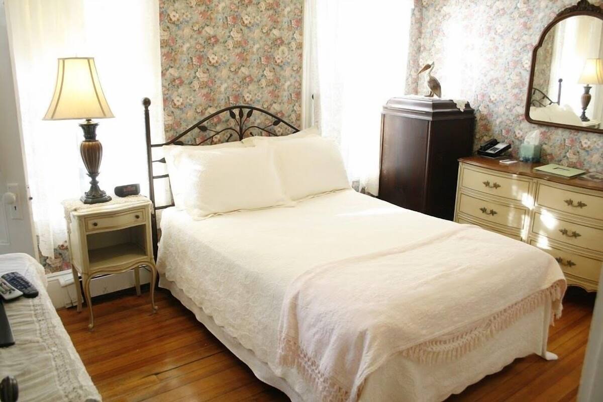 Una camera da letto con un letto, comodino, lampada, cassettiera e specchio.