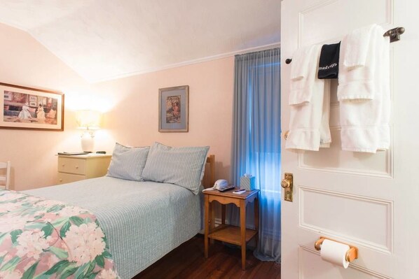A bedroom with a bed, a nightstand, a lamp, a framed picture, and a door with towels hanging on it.