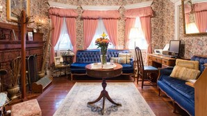A room with a blue sofa, a round coffee table, and a floral wallpaper pattern. - Coolidge Corner Guest House (Brookline)