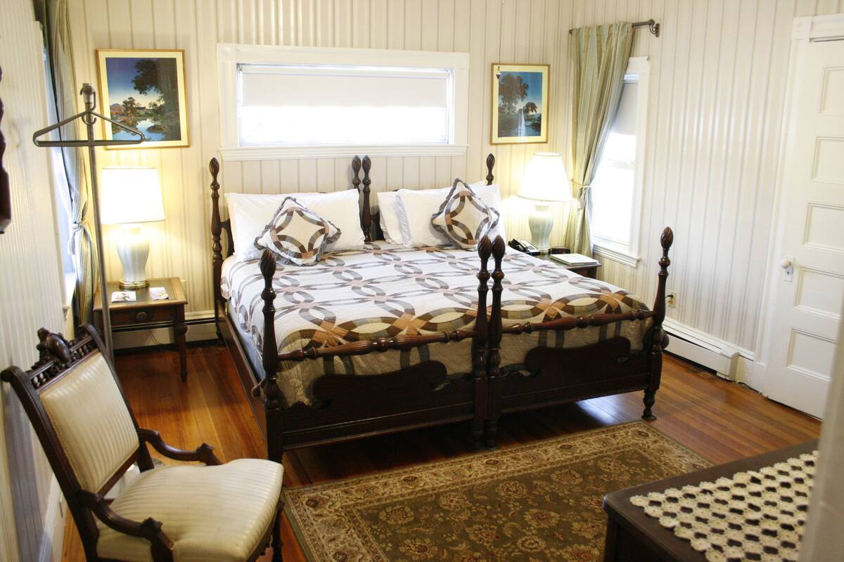 Una camera da letto con un letto a baldacchino, una sedia di legno, un comodino e un tavolino da notte.