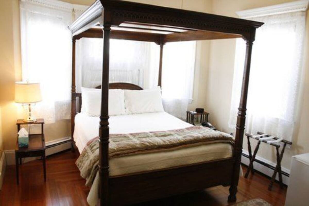 Un letto a baldacchino con struttura in legno, un comodino con una lampada e un piccolo tavolino di appoggio.