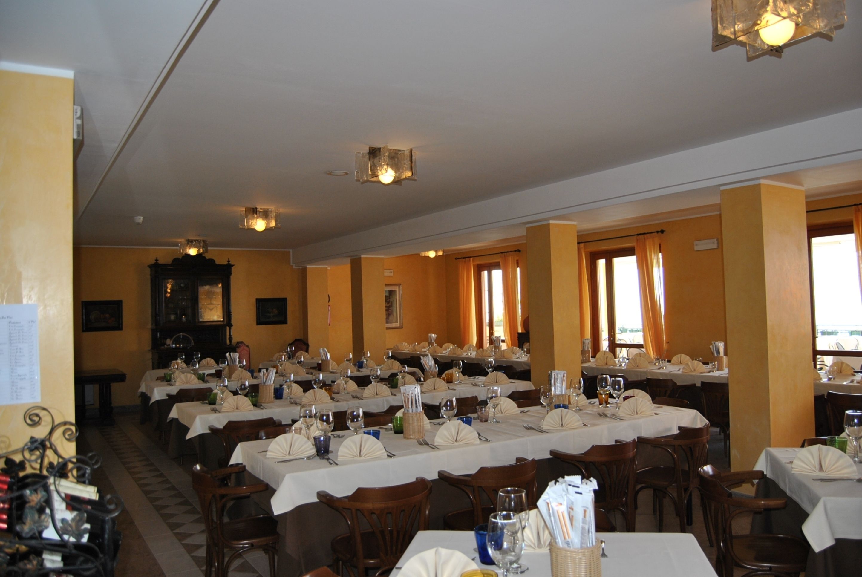 Un amplio comedor con varias mesas dispuestas para un banquete, con sillas de madera y manteles blancos.