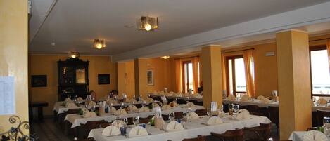 Un amplio comedor con varias mesas dispuestas para un banquete, con sillas de madera y manteles blancos.