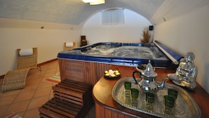 Un cuarto de spa con una bañera de hidromasaje, un banco de madera, una bandeja con copas y una estatua de Buda.
