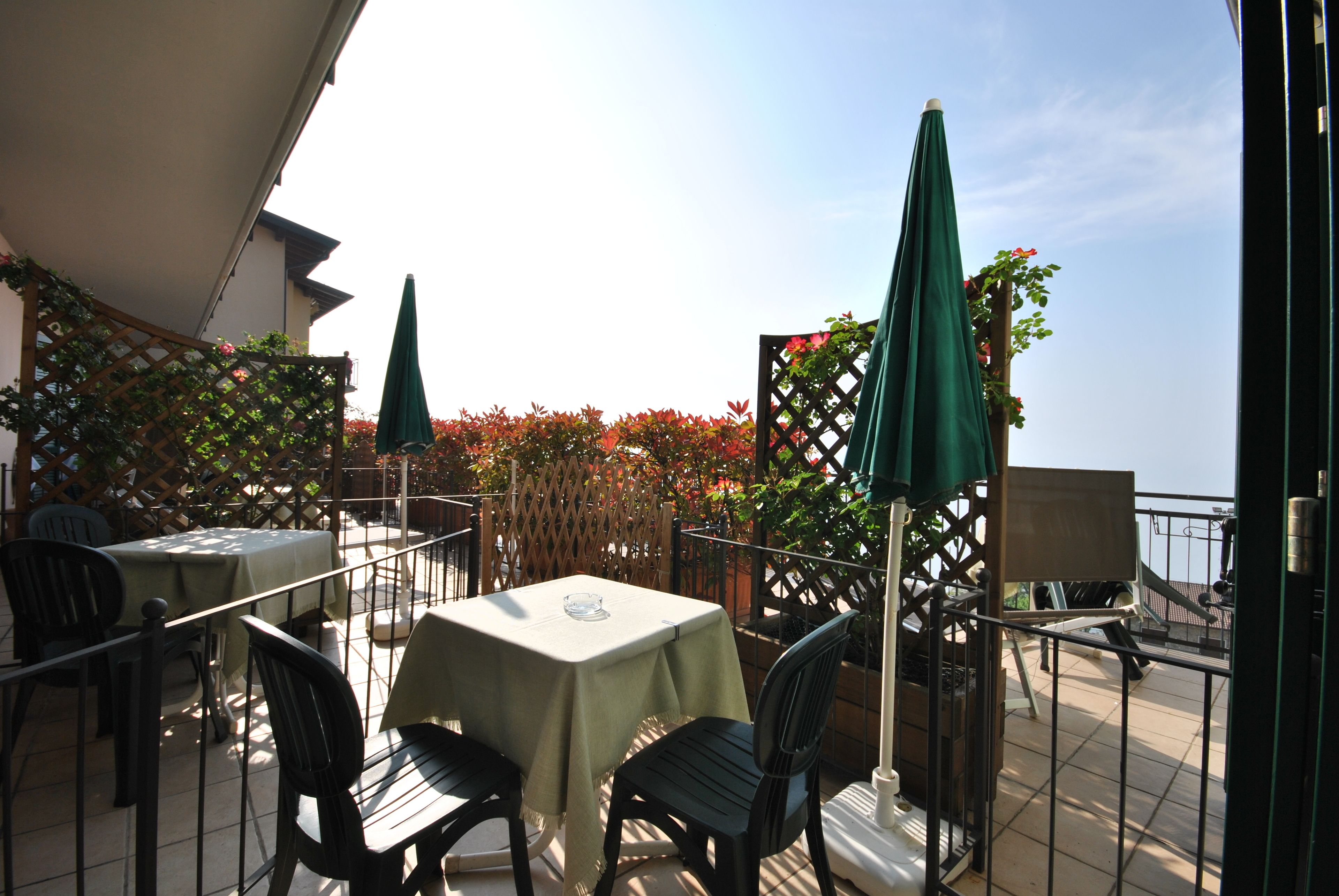 An outdoor patio with tables and chairs, green umbrellas, and a view of the sea.