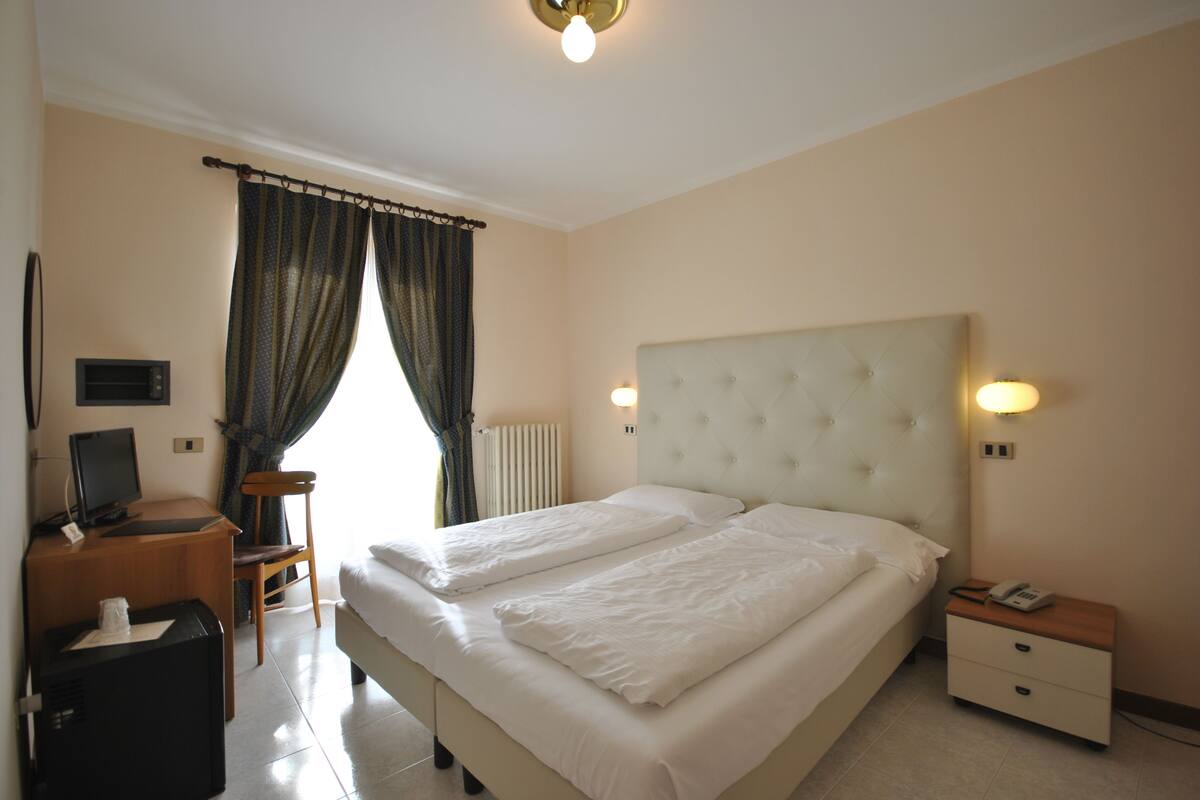 Habitación de hotel con una cama grande, un escritorio con ordenador, una silla y una mesita de noche con teléfono.