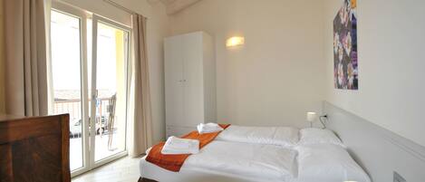 A hotel room with a bed, a wardrobe, a chair, and a balcony with a view.