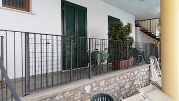 Un balcón con pared de piedra, baranda de metal y mobiliario exterior, incluyendo una mesa y sillas.