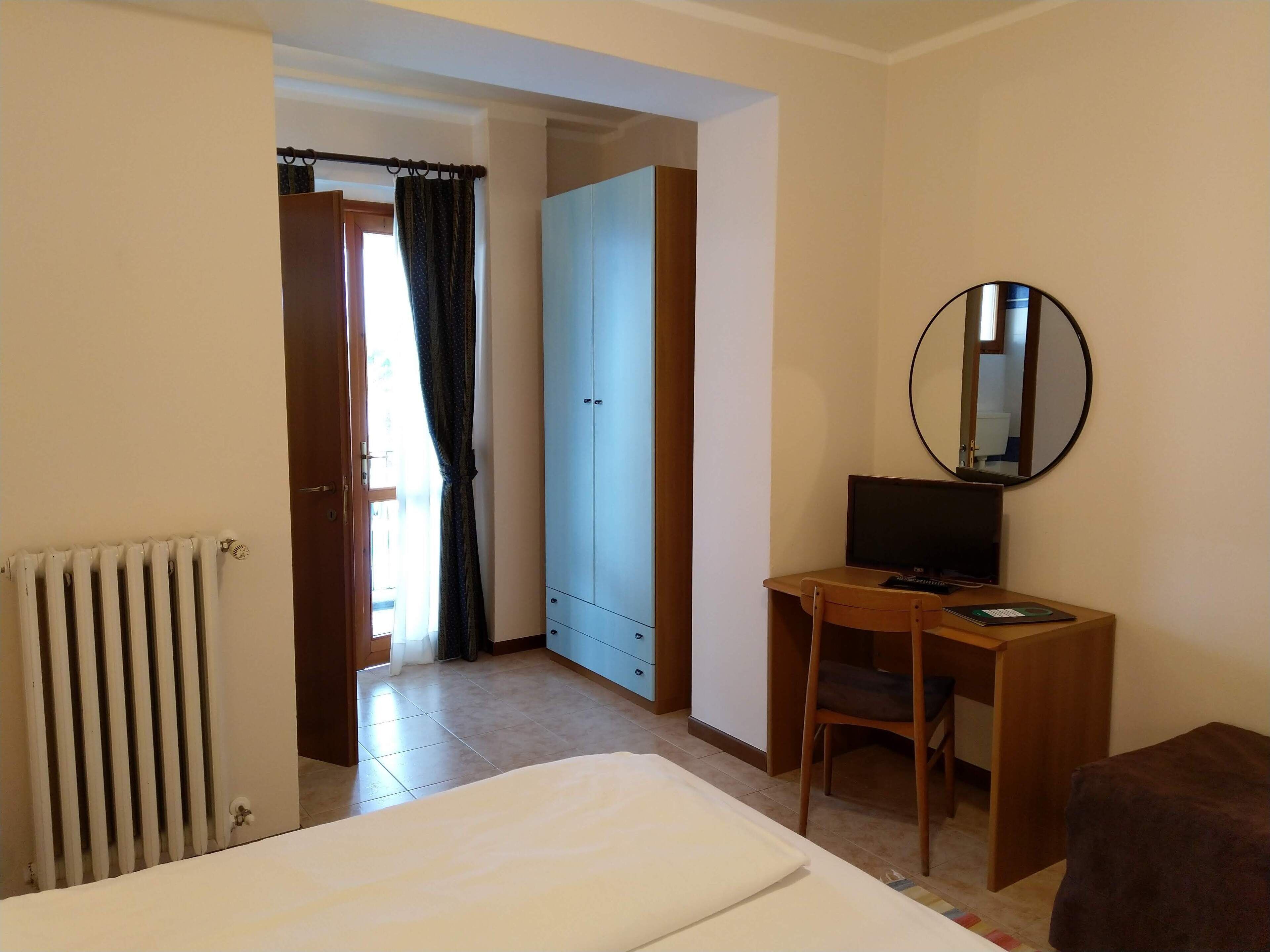 A hotel room with a bed, a desk with a computer, a chair, a wardrobe, and a radiator.