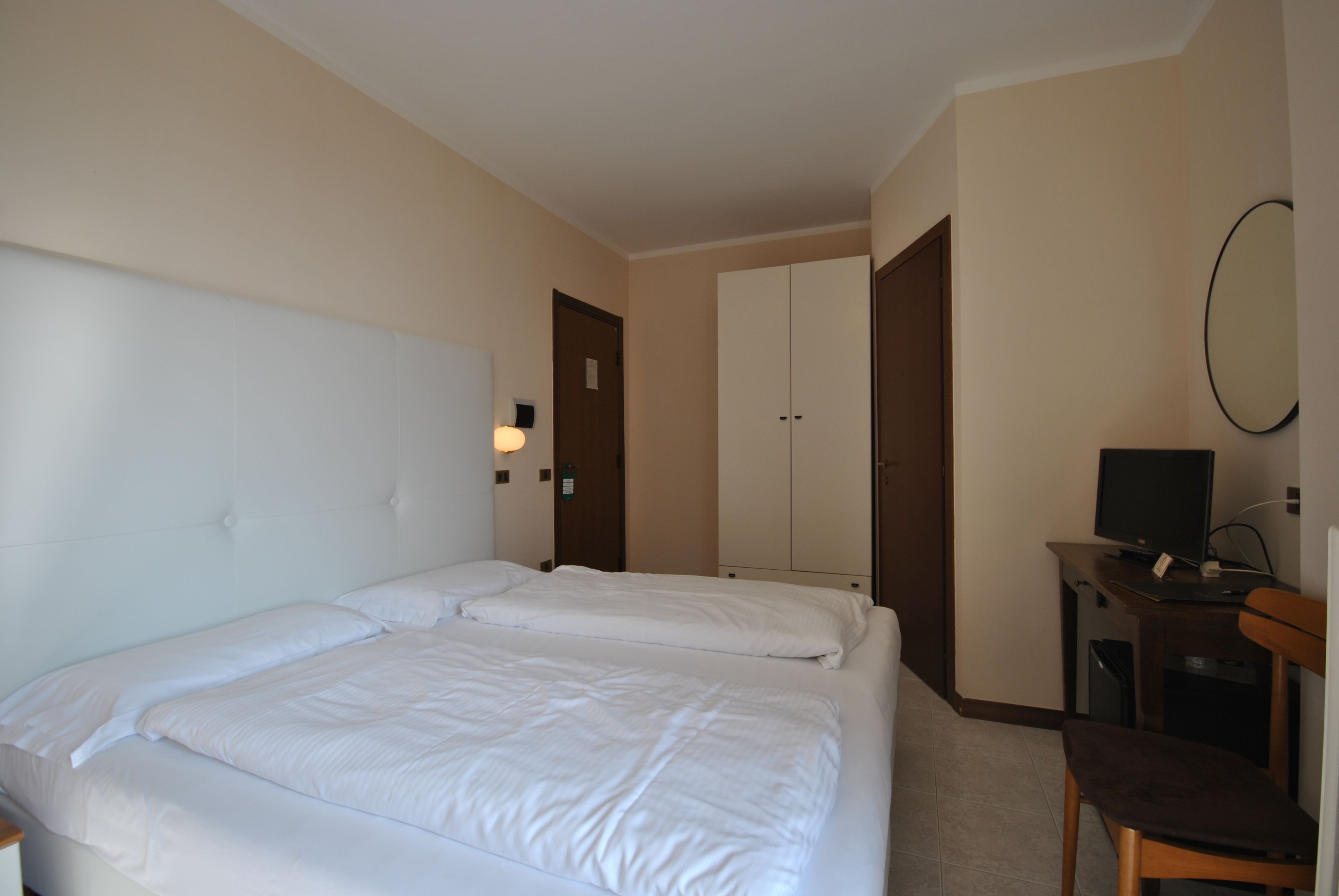 Una camera d'albergo con due letti, una scrivania con un computer e una televisione.