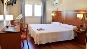 A hotel room with a bed, desk, chair, and a TV mounted on the wall. - Hotel Mari Carmen (Guadix)