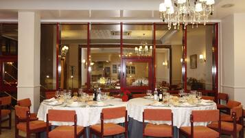 A dining area with tables set for a meal, chairs, and a chandelier.
