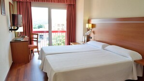 A hotel room with two beds, a desk with a computer, a TV, a balcony with a red railing, and a wooden headboard. - Hotel Mari Carmen (Guadix)