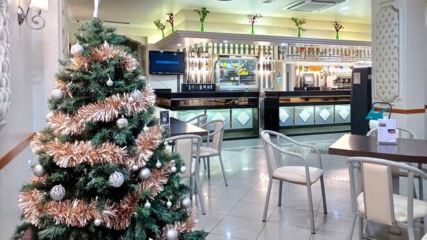 A Christmas tree in a hotel lobby with a bar area in the background. - Hotel Mari Carmen (Guadix)