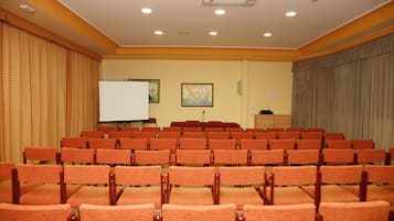 A conference room with rows of orange chairs, a whiteboard, and two framed artworks on the walls.