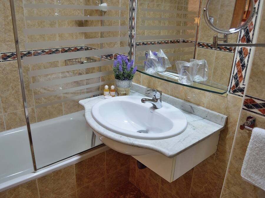 Un baño con un lavamanos blanco, cabina de ducha con mampara de vidrio y un espejo.