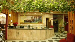 A hotel reception area with a marble counter, a large painting of a vintage car, and a checkered floor. - Hotel Mari Carmen (Guadix)