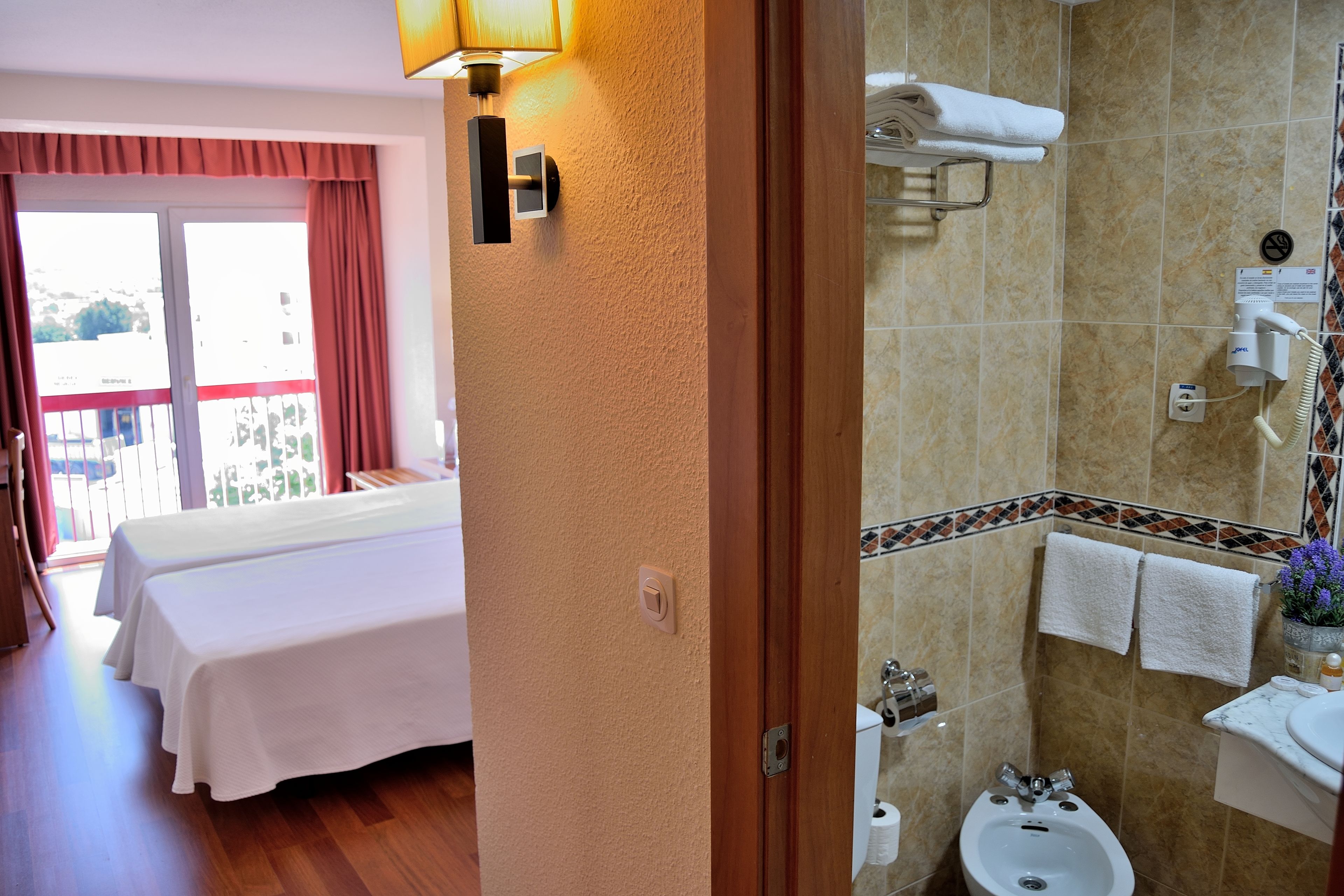 Een hotelkamer met een bed, een badkamer met wastafel en toilet, en een balkon met uitzicht.