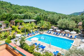 A swimming pool with lounge chairs and umbrellas, surrounded by greenery and buildings. - Villamirella (Centola)